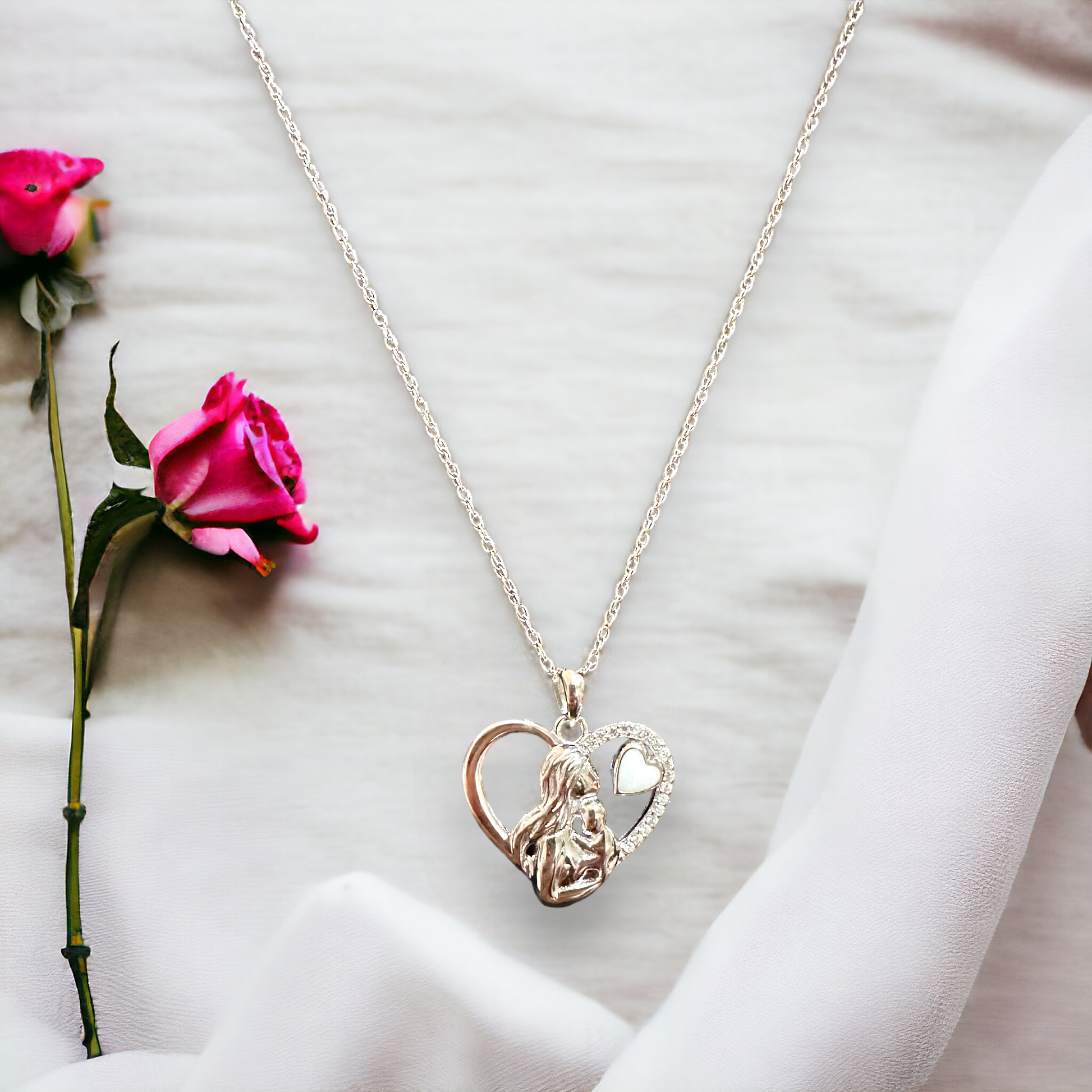 Closeup of the Maternal Embrace heart-shaped sterling silver necklace, featuring an intricate design of a mother and child within the heart, with the child reaching out to his mom, and a small breastmilk heart above them to the right, symbolizing the deep connection and love of motherhood.