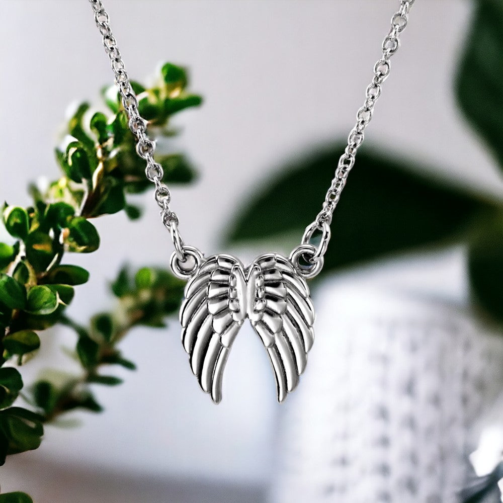  Sterling silver angel wings necklace against a natural green background, reflecting purity and serenity.