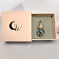 Elegant presentation of the Luminous Moonlight Aurora Opal and Moonstone Necklace in a light pink box with a golden logo.