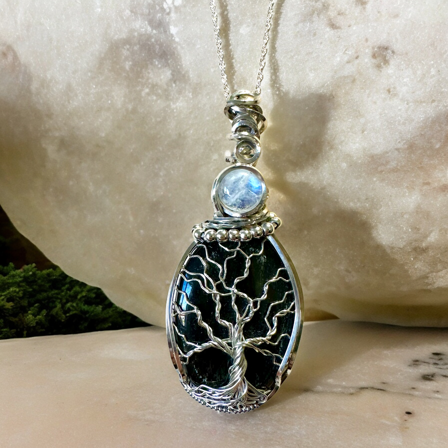 Handcrafted Lunar Reflections Tree of Life Necklace featuring black obsidian and moonstone in sterling silver, against a rock background.