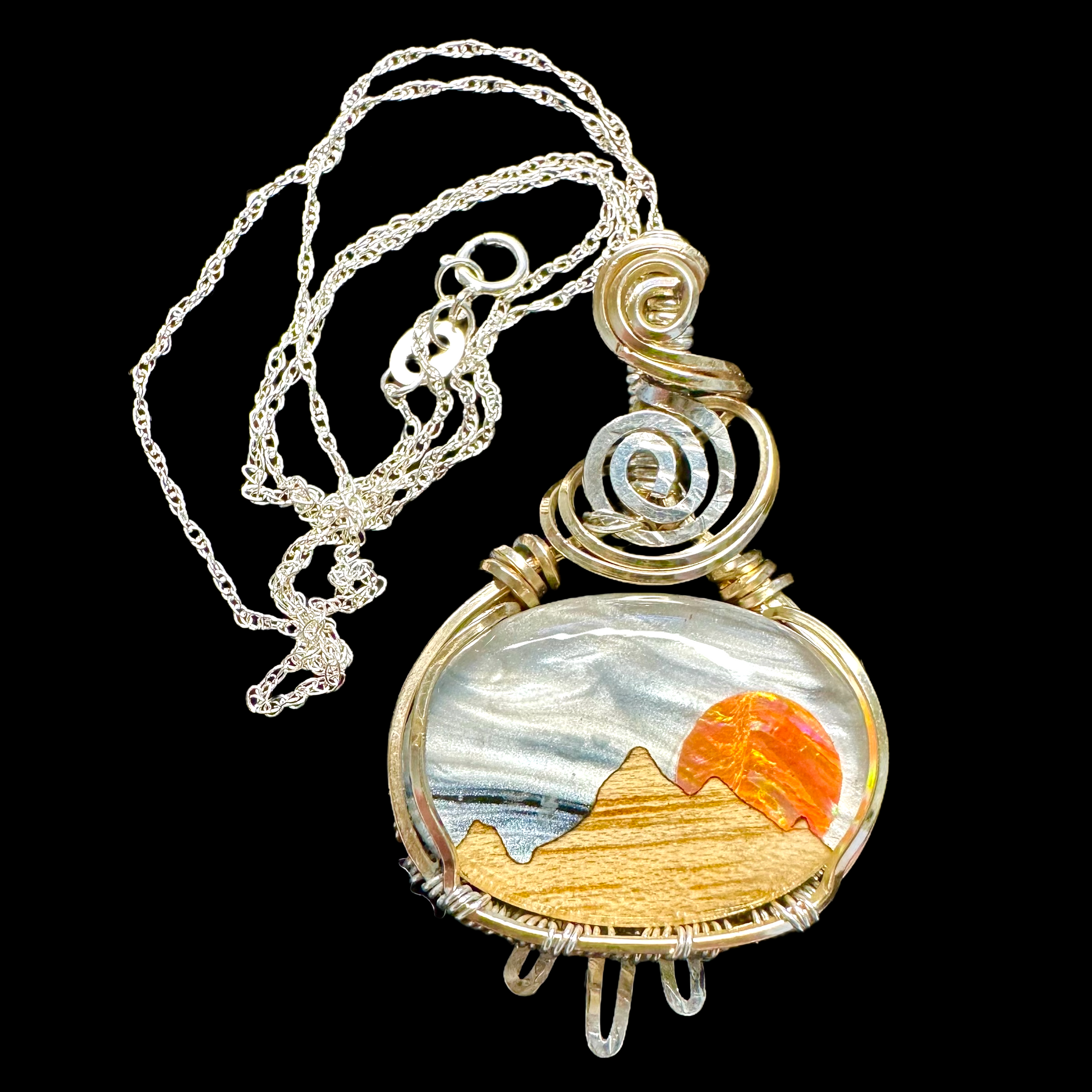 Detailed view of a handcrafted necklace pendant featuring mother of pearl sky and aurora opal sun with a wooden mountain base under a quartz crystal.