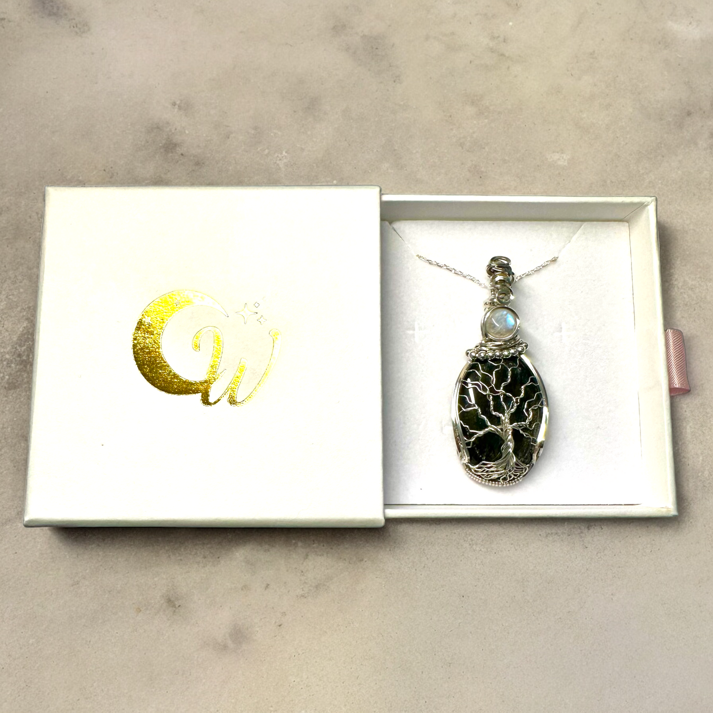 Elegant presentation of the Lunar Reflections Tree of Life Necklace in a white box with shiny golden logo, ready for gifting.