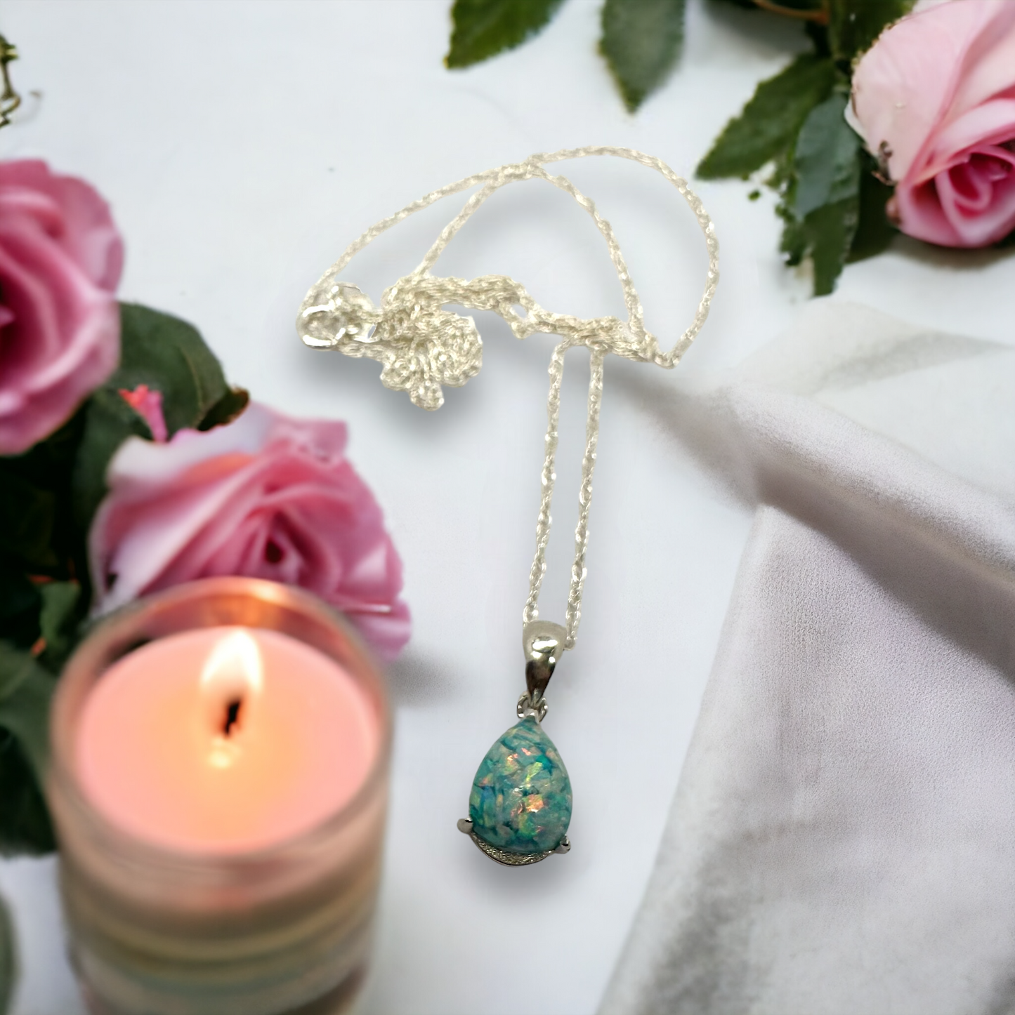 The Whisper Drop sterling silver necklace laid on a table, with a pear-shaped seafoam cremation stone in the setting, showing the full length of the chain, highlighting the pendant's graceful elegance.