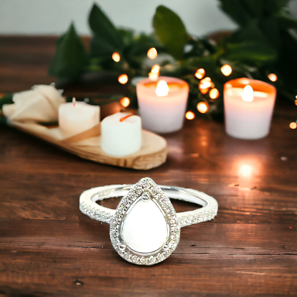 Close-up of the Precious Drop Halo Pear Breastmilk Ring on a table, featuring a white breastmilk stone within a dazzling array of cz stones, representing love's purest form