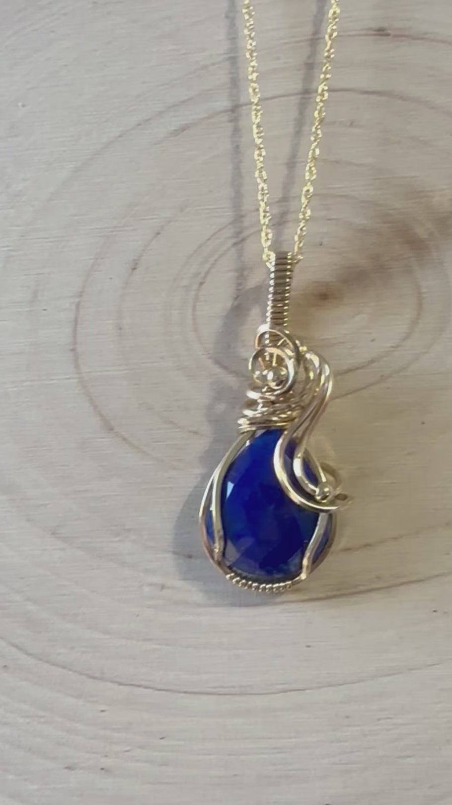 Video displaying the Royal Cascade Lapis Lazuli Teardrop Necklace, focusing on the stone's vibrant blue color and sparkling facets as it moves. The video highlights the necklace's elegant 14k gold filled wire wrapping and the subtle interplay of light, enhancing the gemstone's royal blue hues.